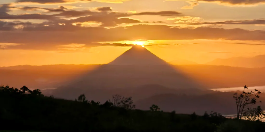 Sunrise behind Arenal Volcano, seen from the Tilarán side, its long shadow cast across the hills toward Lake Arenal